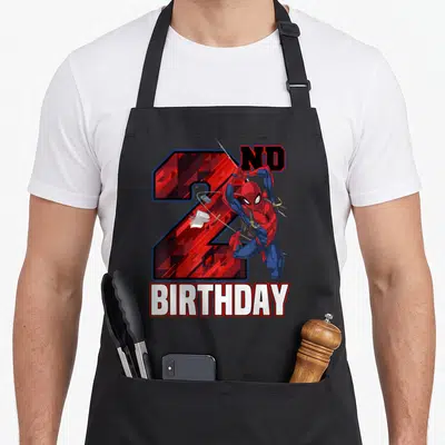 Web 2nd apron - Superhero leaping over red number 2 with ND BIRTHDAY text — shown on a black cotton canvas apron against a white background