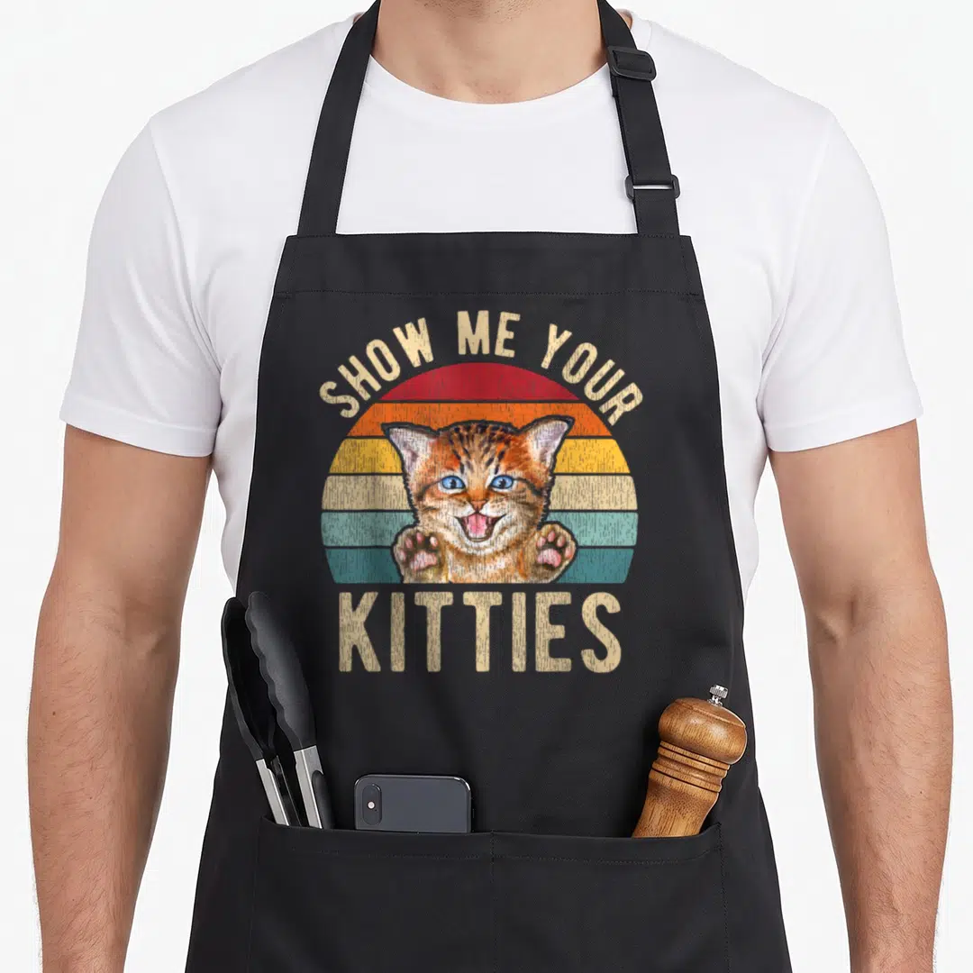 Show kitten kitty cat apron - Retro striped sun with blue-eyed kitten and SHOW ME YOUR KITTIES text in beige — shown on a black cotton canvas apron against a white background