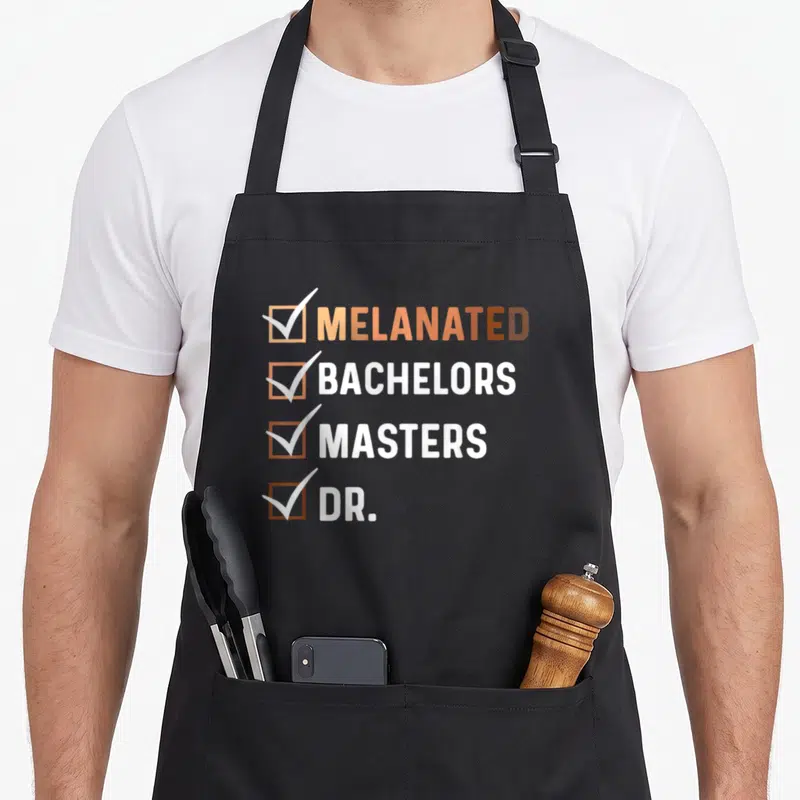 Melanated master apron - Tan brown and white checklist text Melanated Bachelors Masters Dr with checkmarks — shown on a black cotton canvas apron against a white background