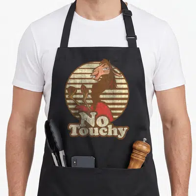 Emperor llama apron - Cartoon goat on striped circle with No Touchy text in brown beige and red — shown on a black cotton canvas apron against a white background