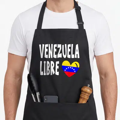 Libre pride apron - VENEZUELA LIBRE text beside a heart filled with yellow blue and red flag stripes and white stars — shown on a black cotton canvas apron against a white background
