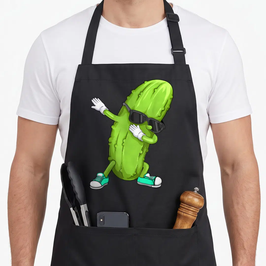 Dabbing dancing pickle apron - Green cartoon pickle wearing sunglasses white gloves and turquoise sneakers in a dab pose — shown on a black cotton canvas apron against a white background
