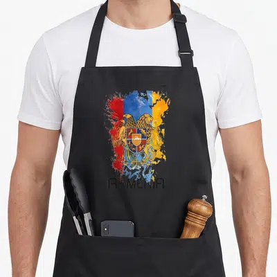 Clothe armenian apron - Coat of arms over red blue and yellow paint splatter with black ARMENIA text — shown on a black cotton canvas apron against a white background