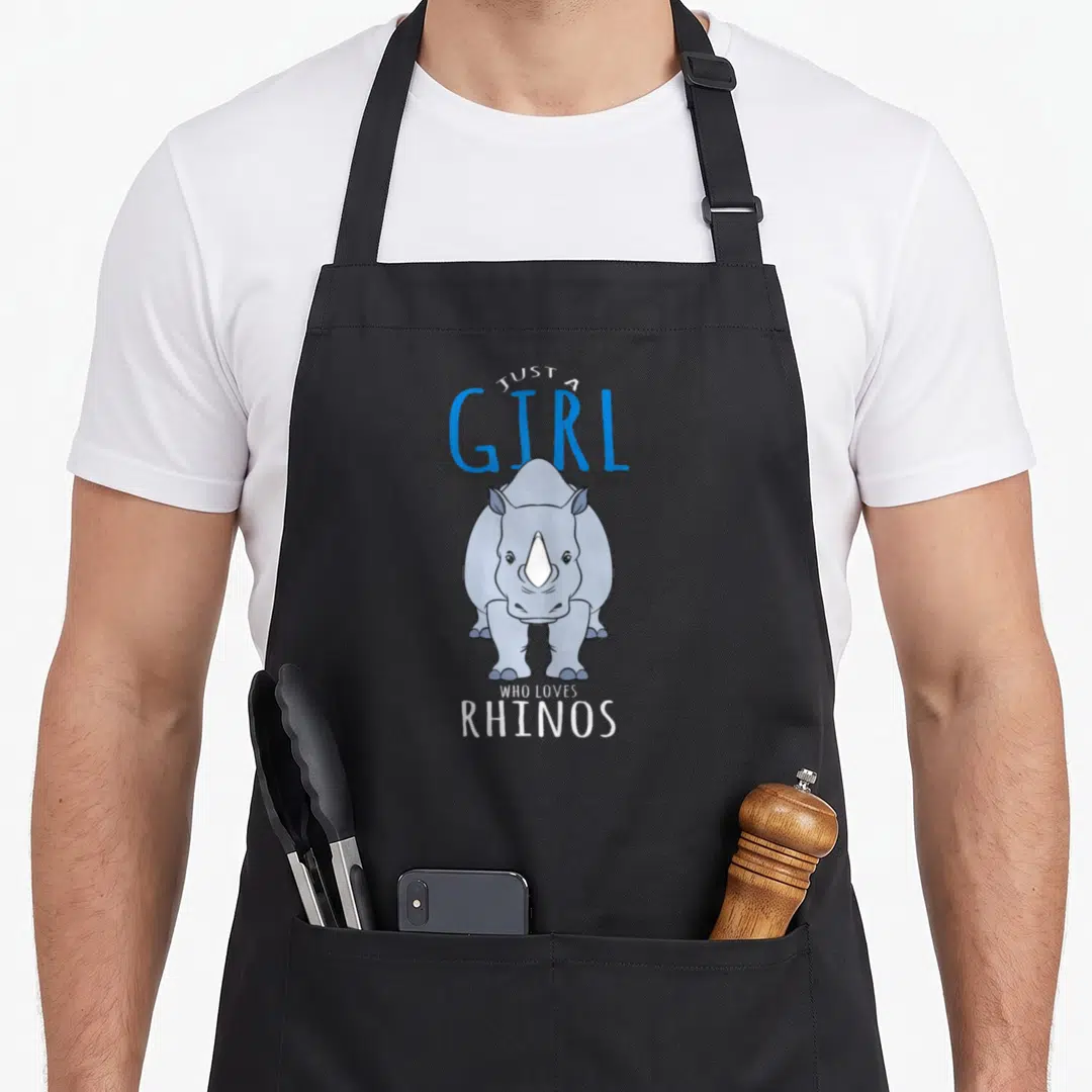 Funny costume rhino mom apron - Cartoon grey rhino with white horn and blue text reading Just A Girl Who Loves Rhinos — shown on a black cotton canvas apron against a white background