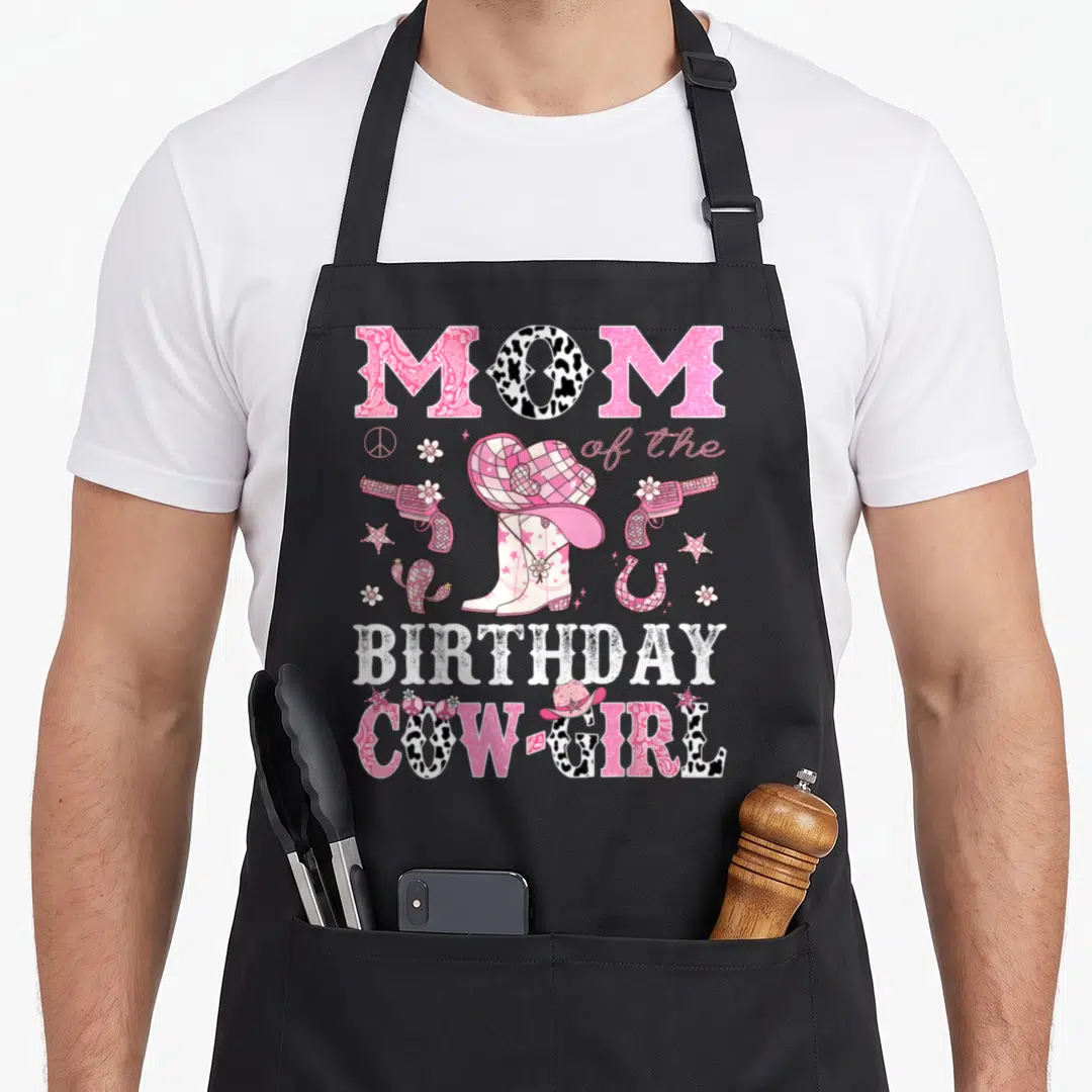 Disco cowgirl aprons - MOM of the BIRTHDAY COW-GIRL text with pink boots, guns, and cactus — shown on a black cotton canvas apron against a white background