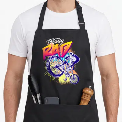 Rad 80s apron - Totally rad text above bmx rider stunt with blue orange yellow purple splatters — shown on a black cotton canvas apron against a white background