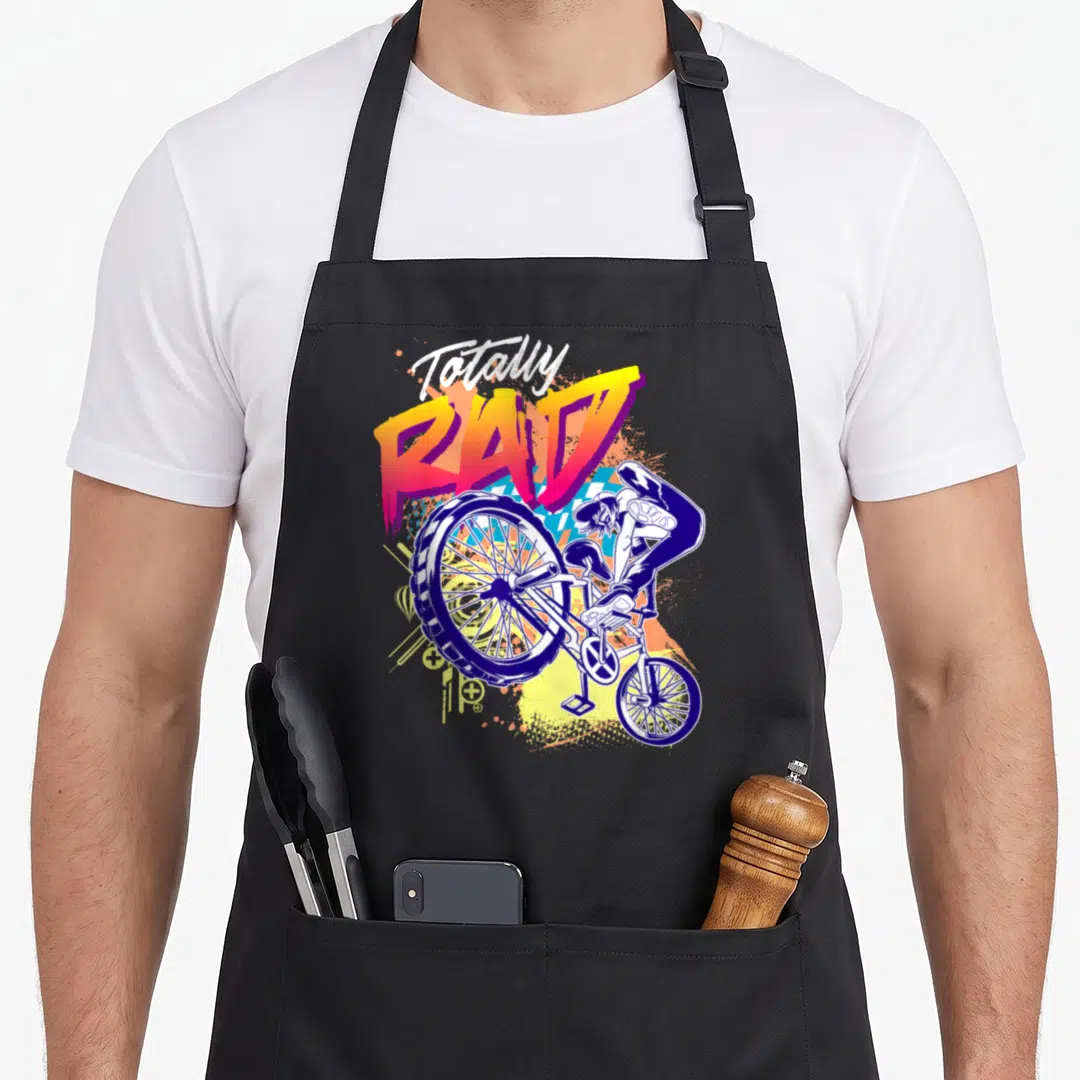 Rad 80s apron - Totally rad text above bmx rider stunt with blue orange yellow purple splatters — shown on a black cotton canvas apron against a white background
