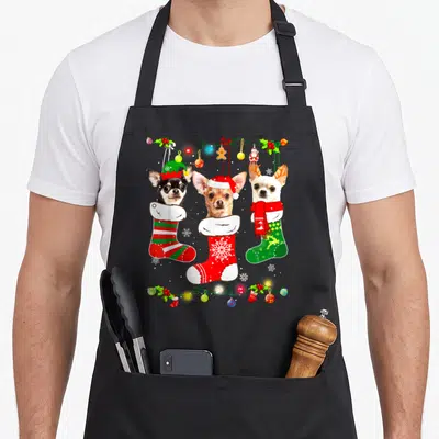 Chihuahua christmas lights apron - Three chihuahuas in red and green stockings framed by Christmas lights and holly — shown on a black cotton canvas apron against a white background