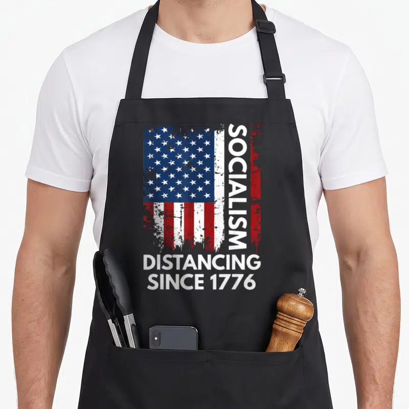 Socialism novelty apron - Distressed USA flag with vertical SOCIALISM text and DISTANCING SINCE 1776 below — shown on a black cotton canvas apron against a white background