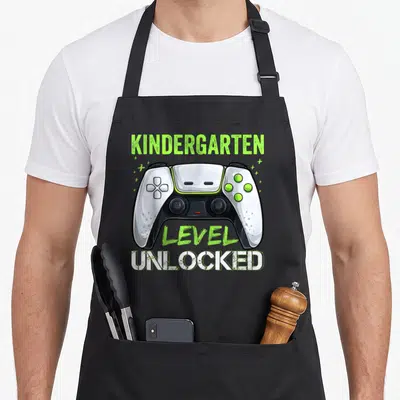 Unlocked love kindergarten apron - White and black game controller with lime green text reading kindergarten level — shown on a black cotton canvas apron against a white background