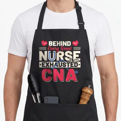 Exhausted nurse apron - Text reading Behind Every Great Nurse Is An Exhausted CNA with hearts and stethoscope — shown on a black cotton canvas apron against a white background