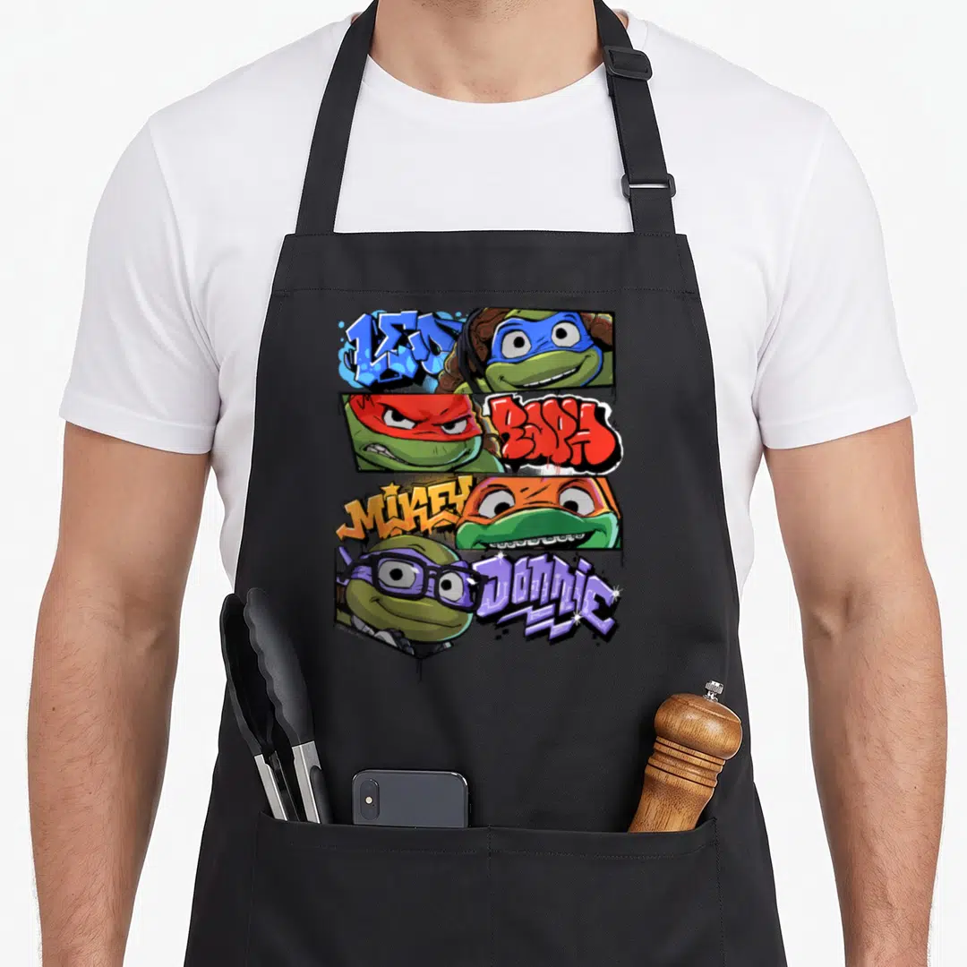 Mutant teenage cooking aprons - Graffiti text Leo Raph Mikey Donnie alongside four cartoon turtle faces in colored masks — shown on a black cotton canvas apron against a white background