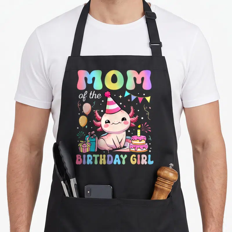 Axolotl family aprons - MOM of the BIRTHDAY GIRL text with pink axolotl, cake, gifts, and bunting in cartoon art — shown on a black cotton canvas apron against a white background