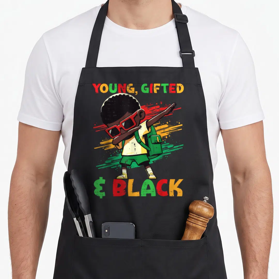 Dab african american aprons - Cartoon boy dabbing with YOUNG GIFTED & BLACK text and paint splashes — shown on a black cotton canvas apron against a white background