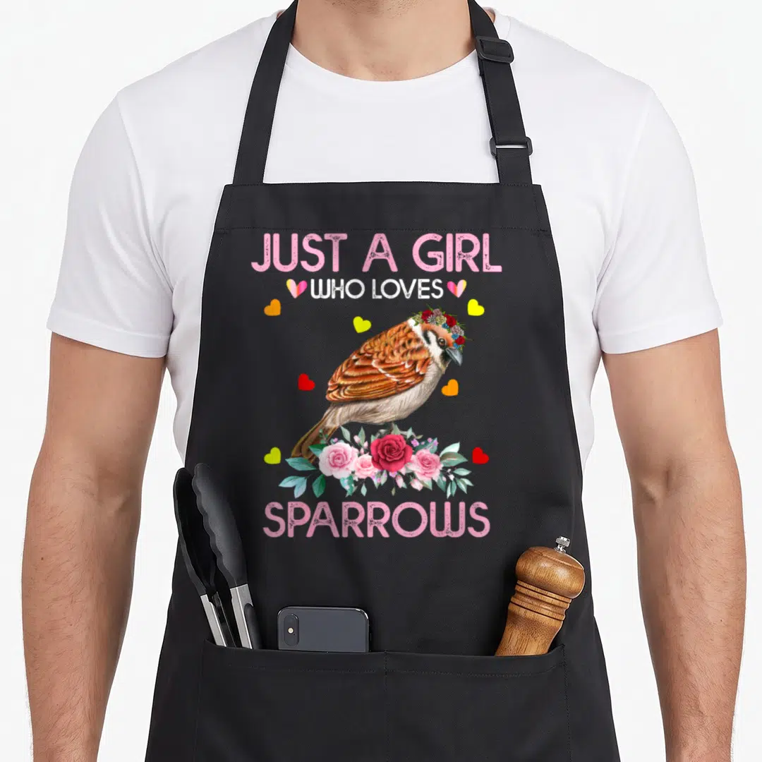 Cute sparrow bird apron - Watercolor sparrow with flower crown standing on pink roses surrounded by hearts and text — shown on a black cotton canvas apron against a white background