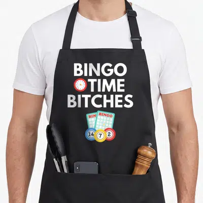 Player bingo apron - Stacked white text Bingo Time Bitches with clock and numbered bingo balls — shown on a black cotton canvas apron against a white background