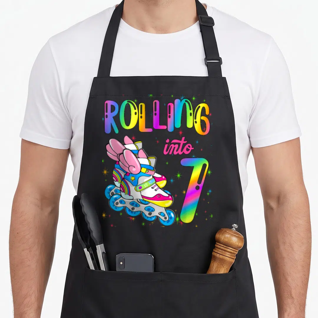 Retro rolling turning apron - Rolling into 7 text with winged rainbow roller skates and scattered stars — shown on a black cotton canvas apron against a white background