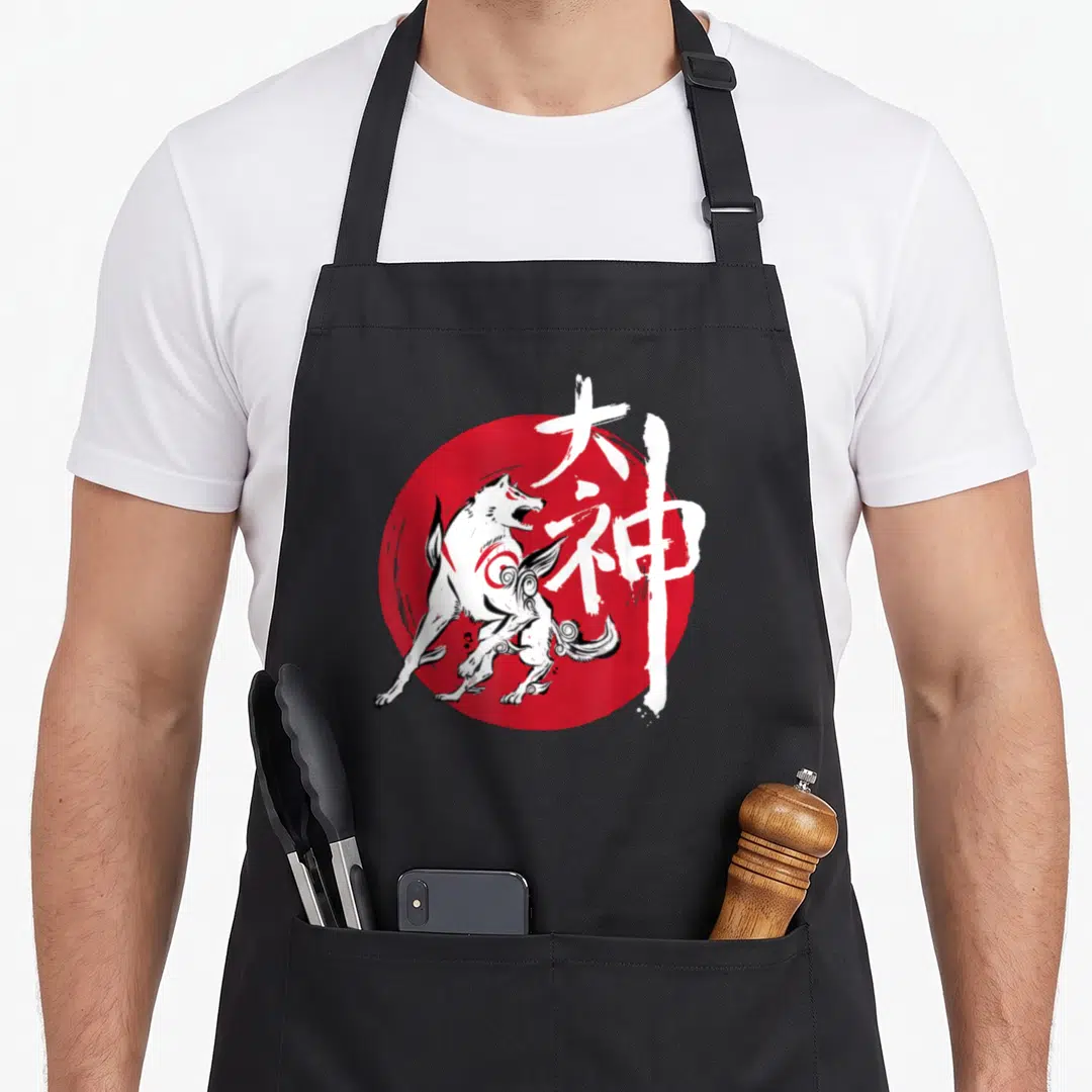 Okami video game apron - White wolf with red swirl on red circle overlaid with white kanji characters — shown on a black cotton canvas apron against a white background