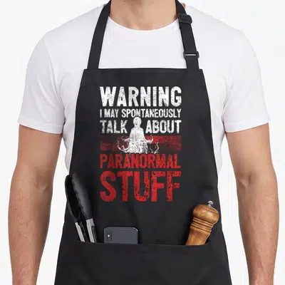 Warning ghost apron - Stacked white and red text surrounding a ghost silhouette behind a red horizontal stripe — shown on a black cotton canvas apron against a white background