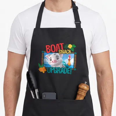 Pua boat apron - Cartoon pig and rooster in frame with BOAT SNACK UPGRADE text and tropical flowers — shown on a black cotton canvas apron against a white background