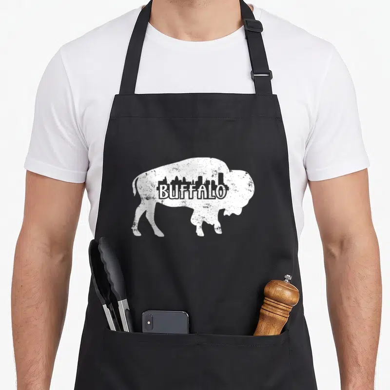 Distressed buffalo apron - White buffalo silhouette with city skyline and text in distressed style — shown on a black cotton canvas apron against a white background