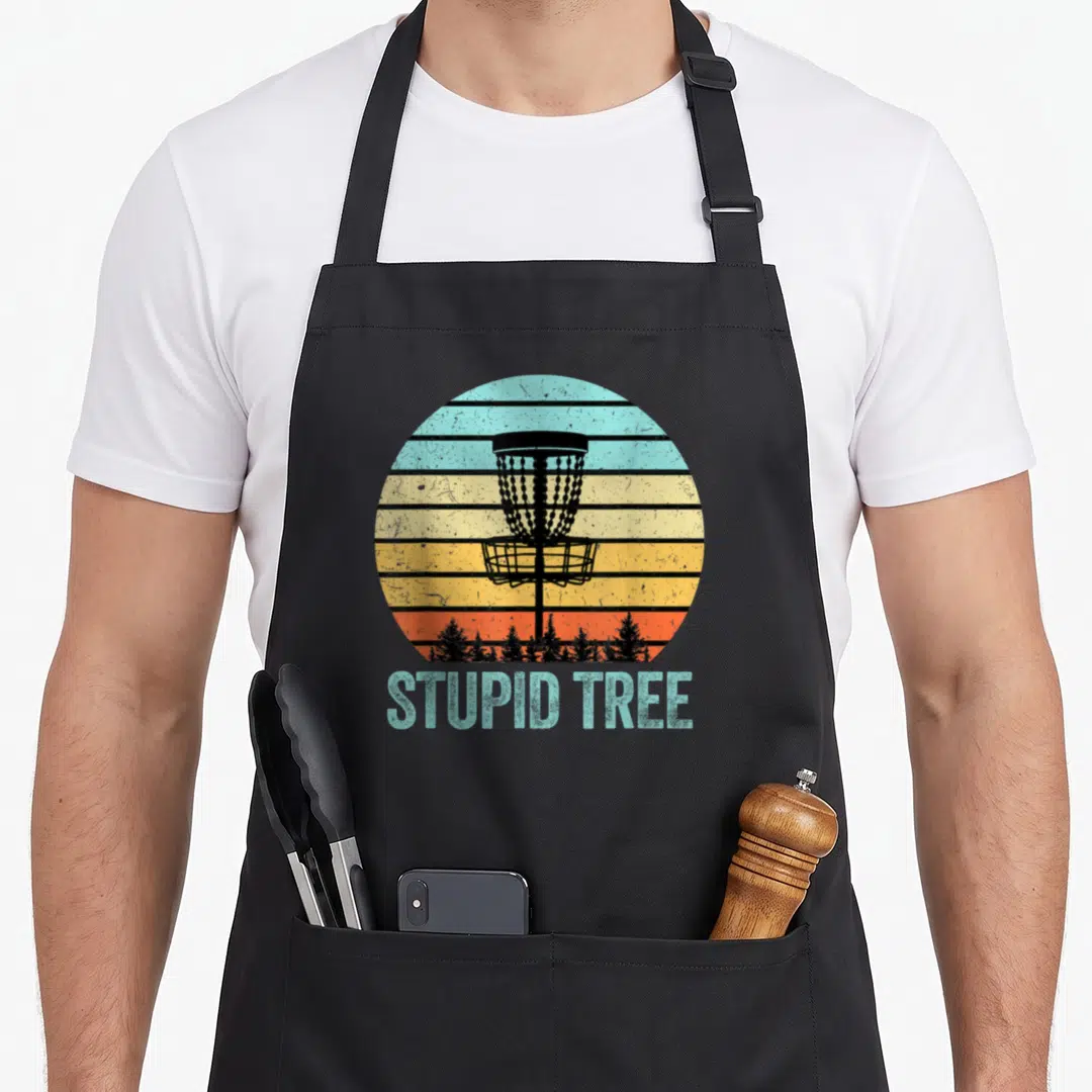 Stupid tree golf apron - Retro disc golf basket silhouette over striped sunset with stacked STUPID TREE text below — shown on a black cotton canvas apron against a white background