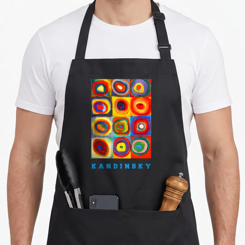 Wassily square apron - Grid of multicolored concentric circles above blue KANDINSKY text — shown on a black cotton canvas apron against a white background