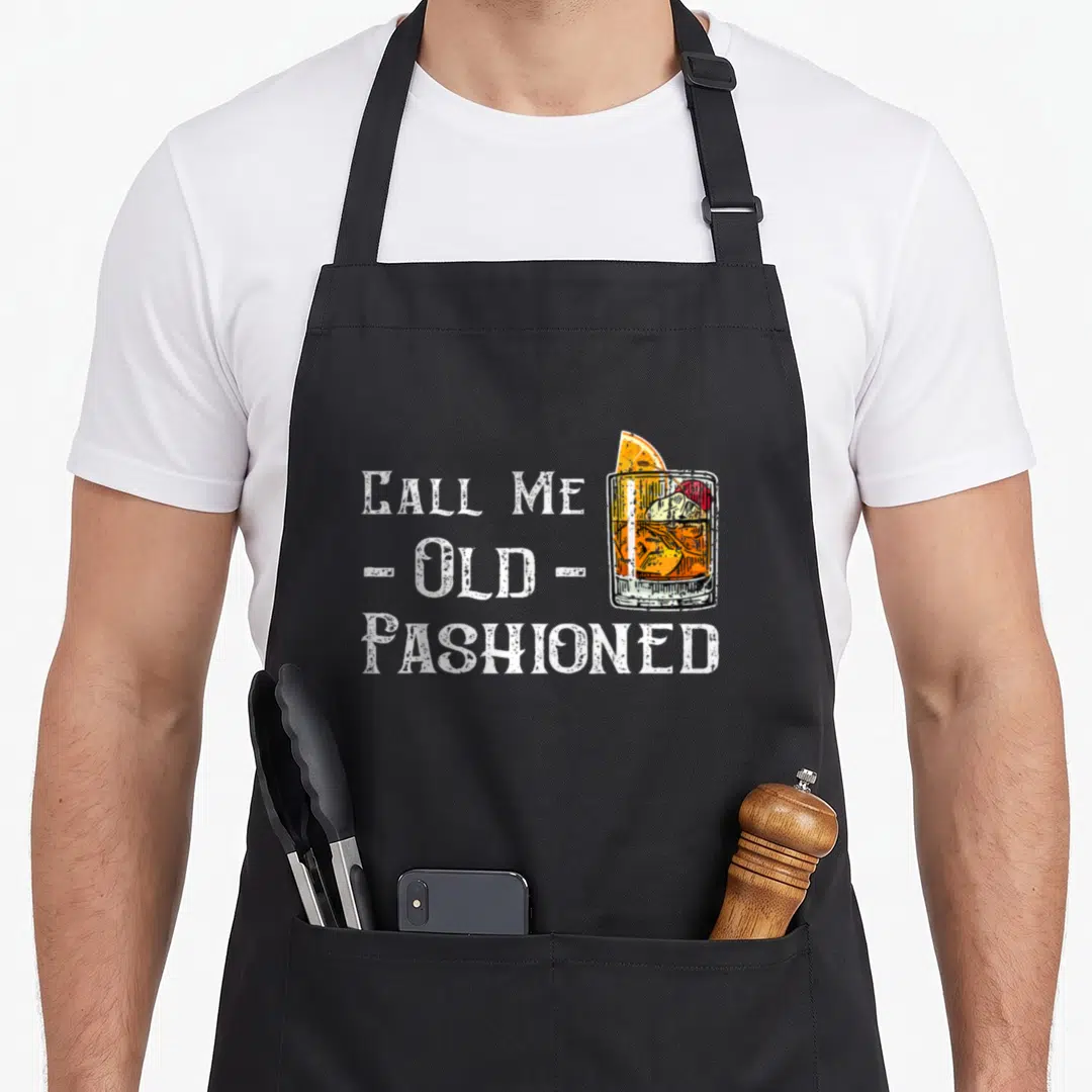 Whiskey old fashioned aprons - Stacked white text CALL ME OLD FASHIONED beside an orange garnished cocktail glass — shown on a black cotton canvas apron against a white background