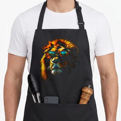 Zoo lion apron - Realistic lion head wearing sunglasses reflecting a landscape in orange and blue — shown on a black cotton canvas apron against a white background