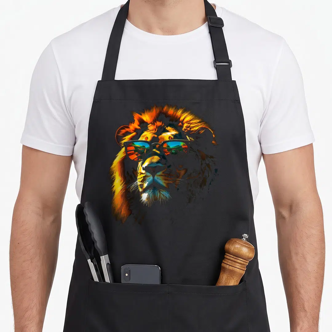 Zoo lion apron - Realistic lion head wearing sunglasses reflecting a landscape in orange and blue — shown on a black cotton canvas apron against a white background