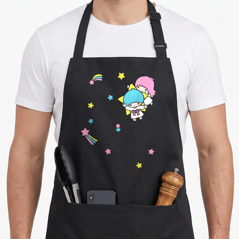 Twin rainbow apron - Two cartoon angels with pink and blue hair surrounded by shooting stars in pink, blue, yellow — shown on a black cotton canvas apron against a white background