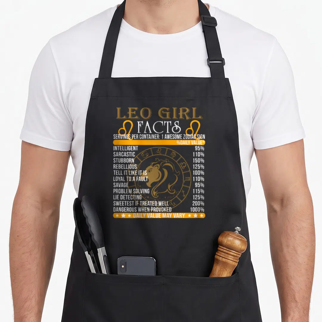 Fact zodiac aprons - Leo Girl Facts nutrition label print with lion icon and orange white text — shown on a black cotton canvas apron against a white background