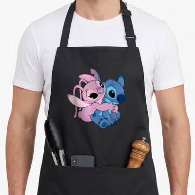 Hugging angels in aprons - Pink Angel hugging blue Stitch cartoon illustration — shown on a black cotton canvas apron against a white background