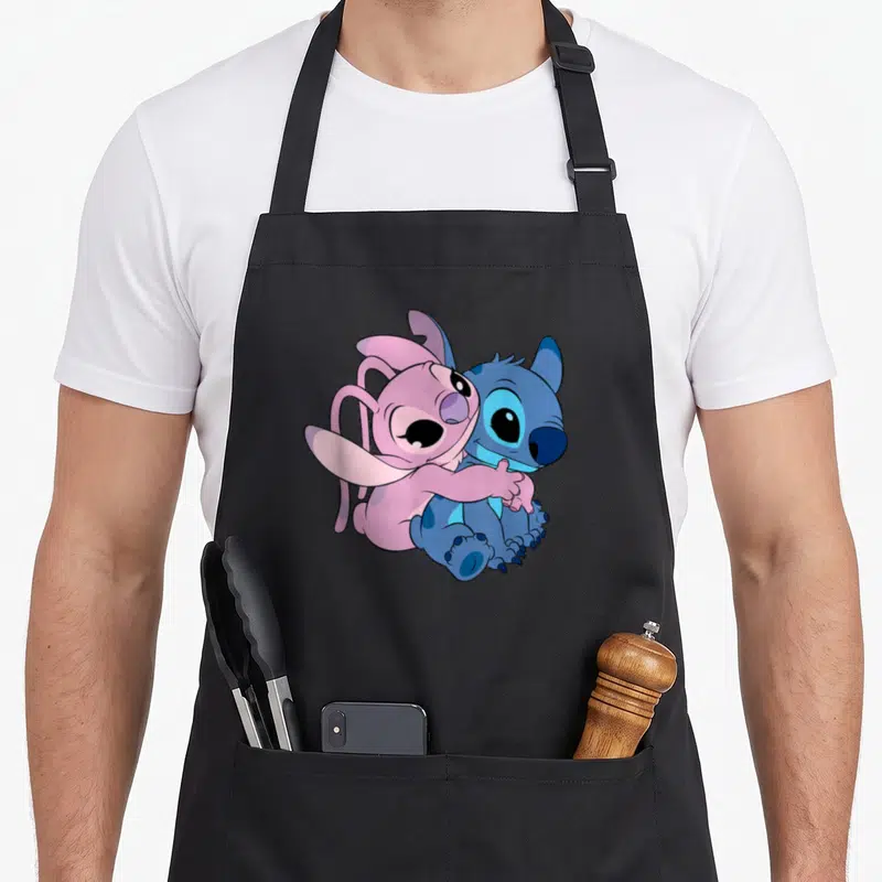 Hugging angels in aprons - Pink Angel hugging blue Stitch cartoon illustration — shown on a black cotton canvas apron against a white background