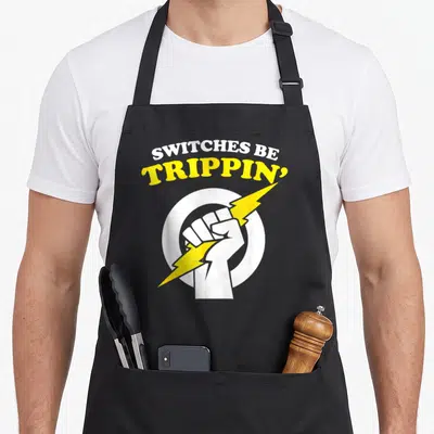 Trippin electrician apron - White fist gripping yellow lightning bolt under arched text on black bib — shown on a black cotton canvas apron against a white background