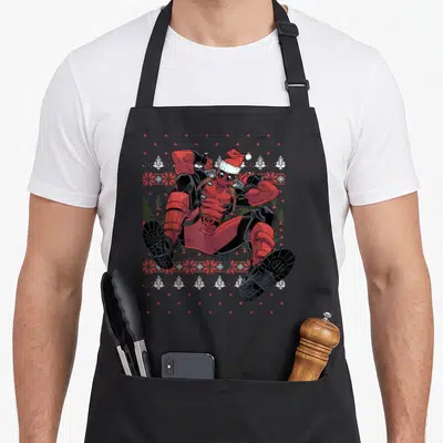 Santa ugly christmas apron - Deadpool in dynamic pose wearing Santa hat against red and white Christmas sweater pattern — shown on a black cotton canvas apron against a white background