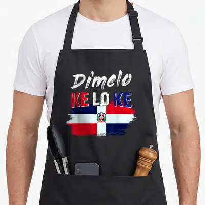 Dimelo dominican apron - Dímelo KE LO KE text over distressed Dominican flag in red white blue — shown on a black cotton canvas apron against a white background
