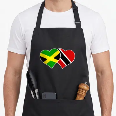 Jamaican trinidadian apron - Two overlapping hearts displaying Jamaican and Trinidad and Tobago flag patterns in green — shown on a black cotton canvas apron against a white background