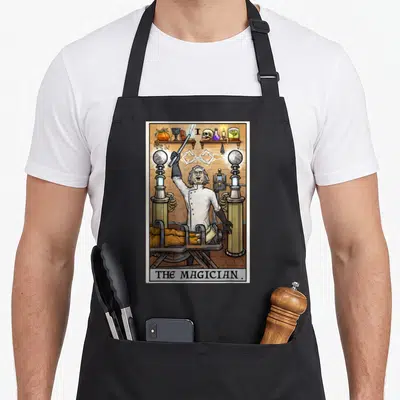 Mad halloween apron - The Magician tarot card as mad scientist with tesla coils, shelf of occult items, and body — shown on a black cotton canvas apron against a white background