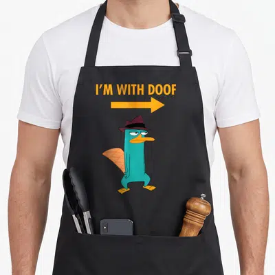 Phineas platypus apron - I'M WITH DOOF text, orange arrow, teal platypus in brown fedora with orange tail — shown on a black cotton canvas apron against a white background