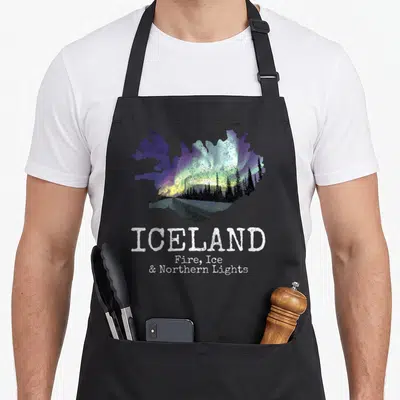 Fire icelandic apron - Distressed Iceland map with aurora borealis and stacked white text reading Fire Ice Northern — shown on a black cotton canvas apron against a white background