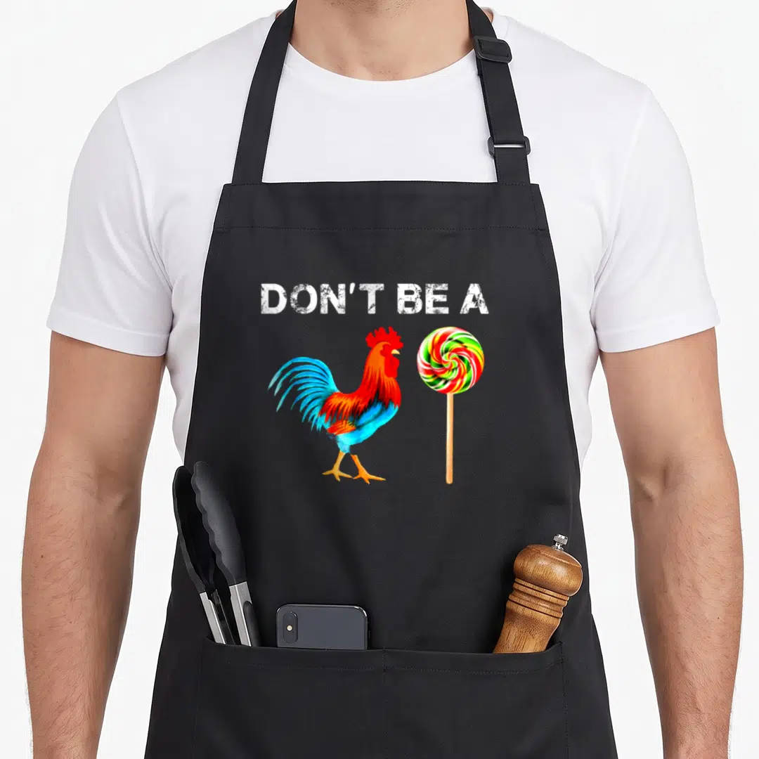 Sucker father day apron - Watercolor rooster and rainbow lollipop below white text DON'T BE — shown on a black cotton canvas apron against a white background