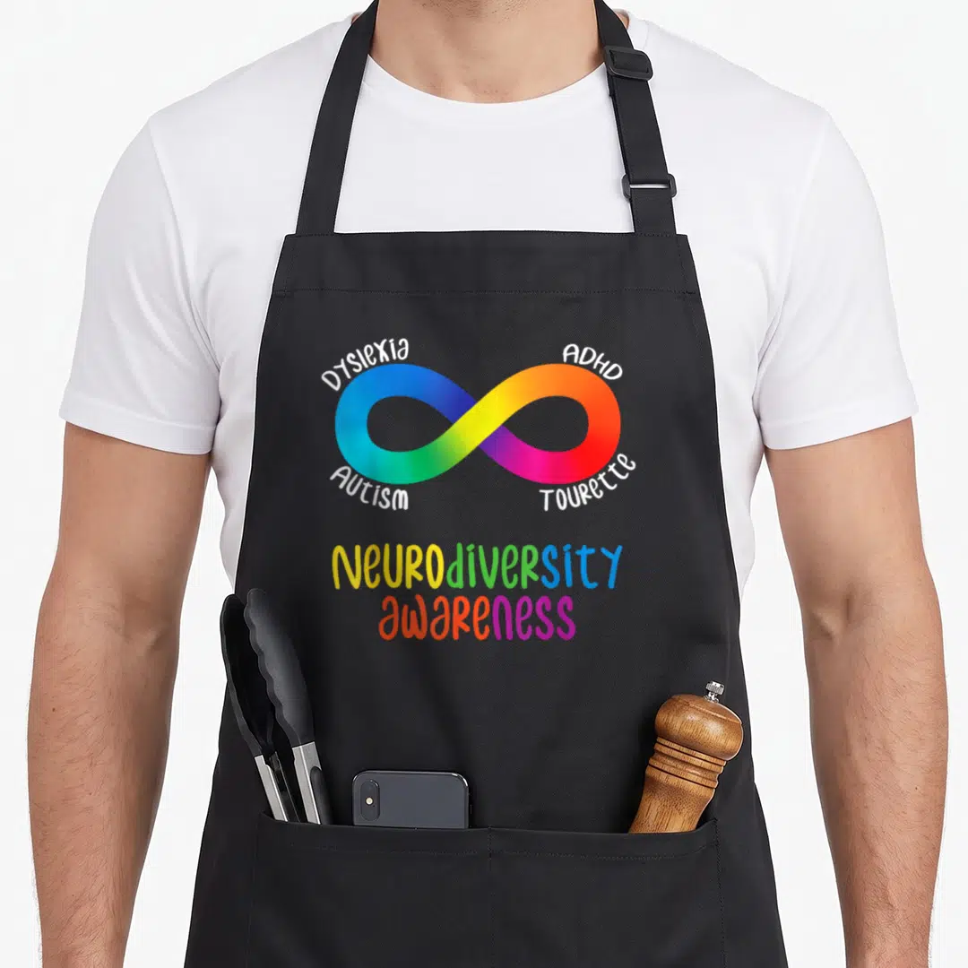 Neurodiversity tourette awareness apron - Rainbow infinity symbol surrounded by Dyslexia ADHD Autism Tourette text — shown on a black cotton canvas apron against a white background