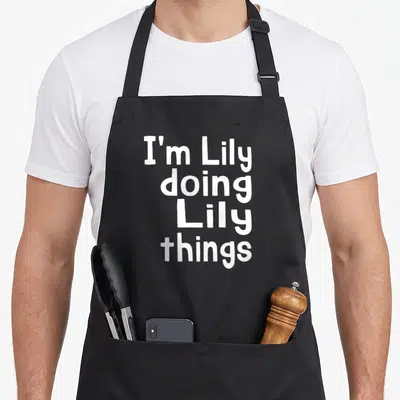 Doing white lily apron - White stacked text reading I'm Lily doing Lily things — shown on a black cotton canvas apron against a white background