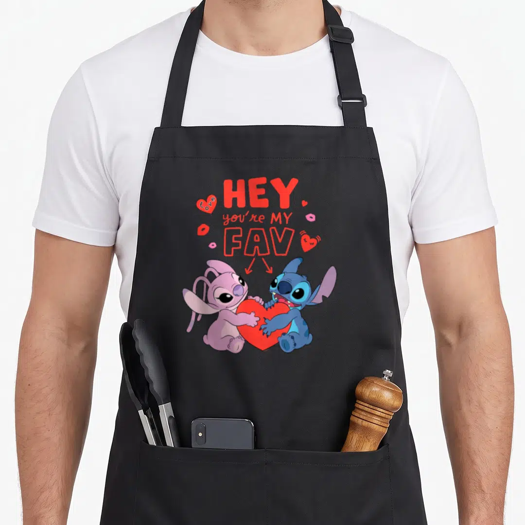 Stitch angels in aprons - Stitch and Angel hugging red heart below stacked HEY you're MY FAV text with hearts and lips — shown on a black cotton canvas apron against a white background