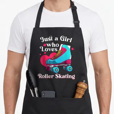Skating birthday for kids roller skates apron - Cartoon blue roller skate over pink heart with white text Just a Girl — shown on a black cotton canvas apron against a white background