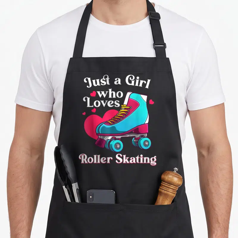 Skating birthday for kids roller skates apron - Cartoon blue roller skate over pink heart with white text Just a Girl — shown on a black cotton canvas apron against a white background