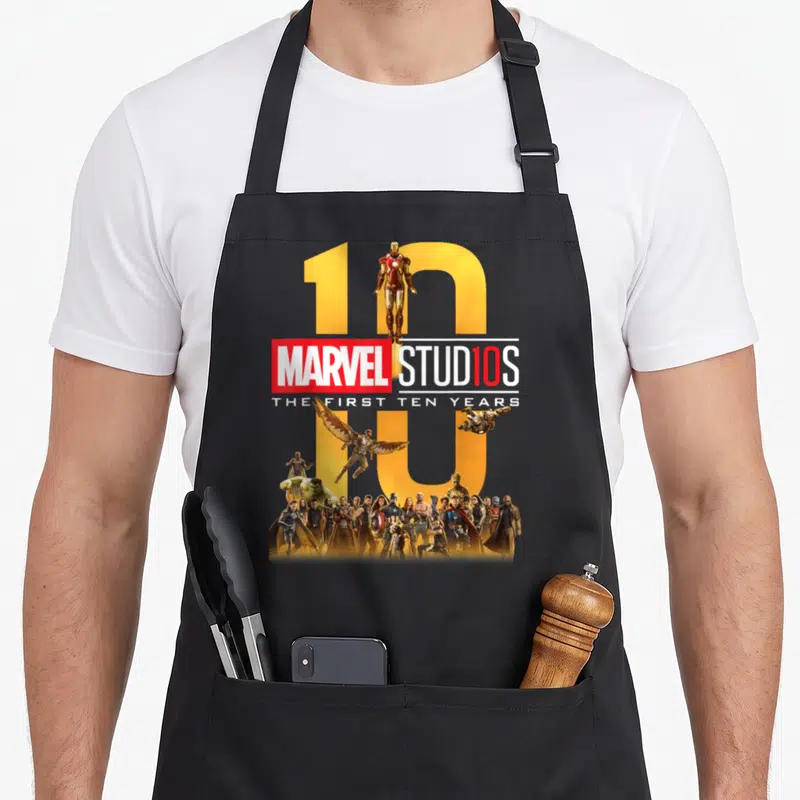 Ten novelty apron - Marvel Studios first ten years logo with cast in yellow red white blue photo style — shown on a black cotton canvas apron against a white background