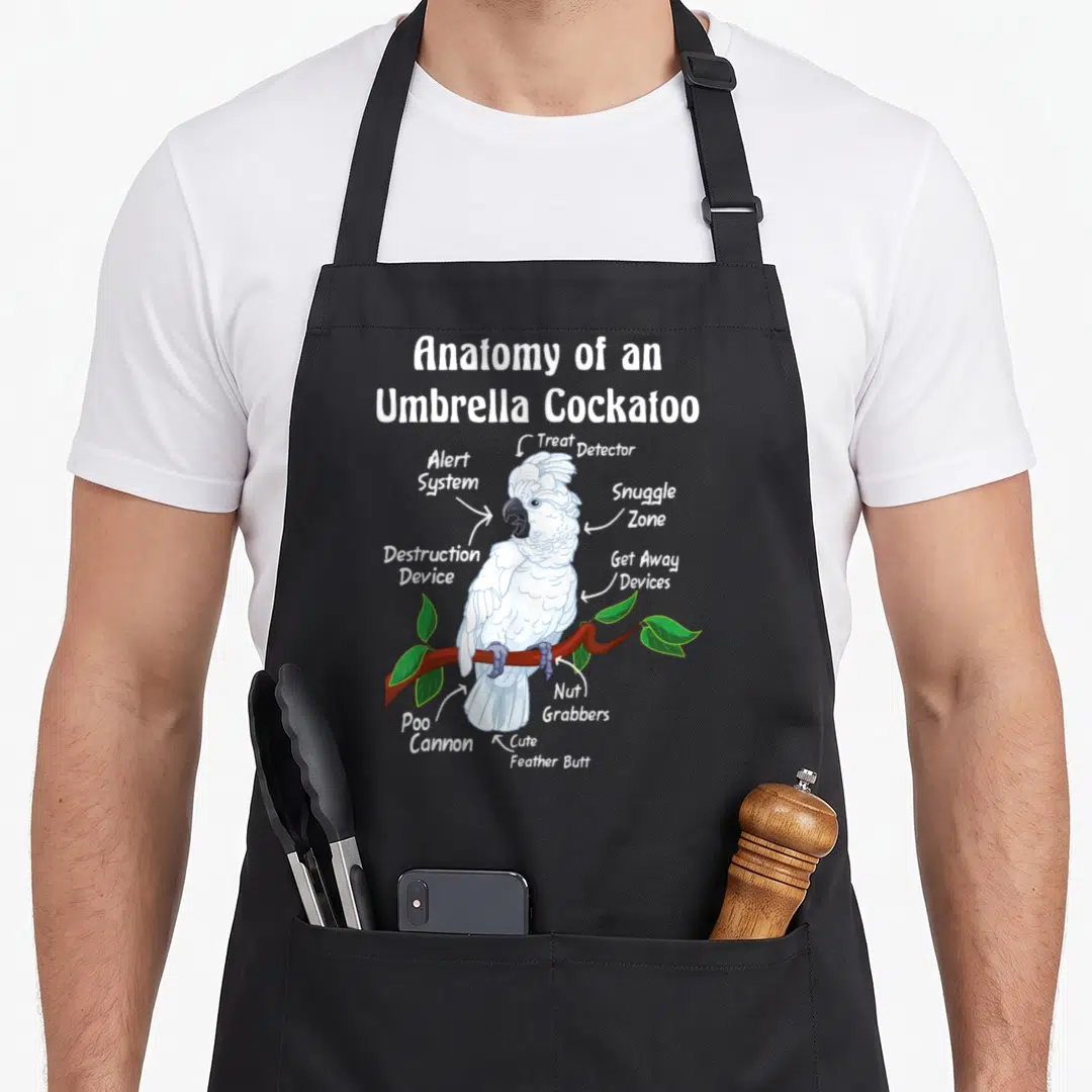 Parrot anatomy apron - Umbrella Cockatoo diagram with labels Poo Cannon Snuggle Zone and Nut Grabbers pointing to body — shown on a black cotton canvas apron against a white background