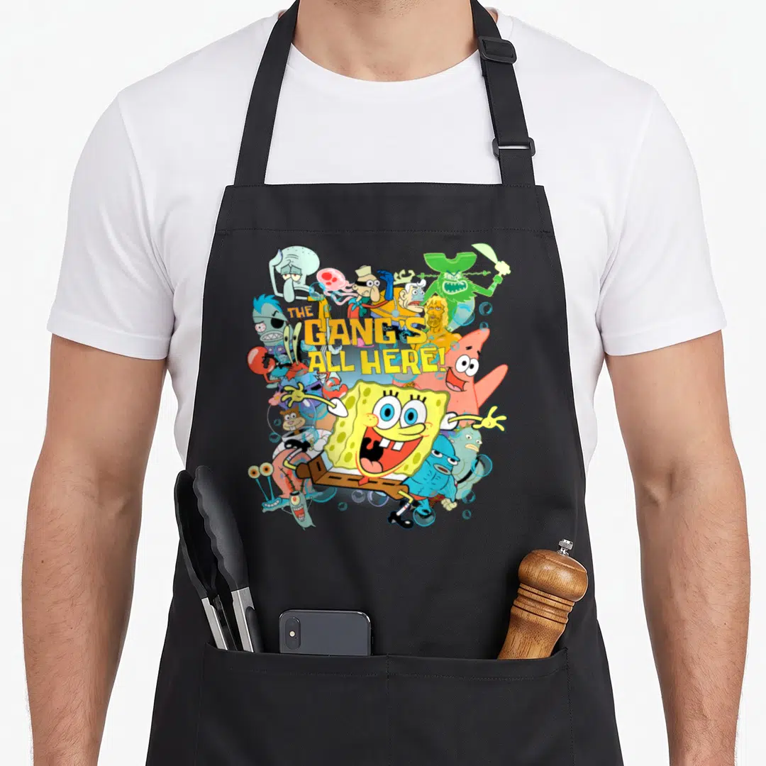 Gang novelty apron - THE GANG'S ALL HERE! text over yellow blue pink and green cartoon characters — shown on a black cotton canvas apron against a white background